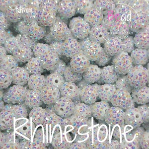 Puede incluir: Primer plano de un montón de cuentas redondas blancas con diamantes de imitación iridiscentes. Las cuentas miden aproximadamente 14 mm de diámetro. Las cuentas son perfectas para la elaboración de joyas, manualidades y decoración del hogar.