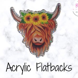 Pode incluir: Flatback de acrílico com uma vaca das Terras Altas com uma coroa de girassóis. A vaca tem pelo castanho-avermelhado e um nariz rosa claro. As bordas são delineadas com glitter prateado. O texto "Acrylic Flatbacks" está na parte inferior.