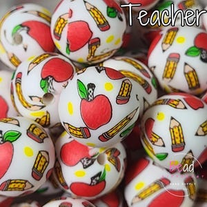 May include: White round beads with red apples, yellow pencils, and green leaves. The word "Teacher" is written in black script across the top. These beads are ideal for crafting projects.