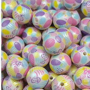 May include: A pile of acrylic beads, each with a white base and decorated with pink, purple, yellow, and blue patterns. The beads are round with a hole for threading. The word "ACRYLIC" is written vertically in pink.