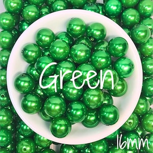 May include: A collection of round, shiny, emerald green beads with a smooth finish. The beads are piled together, with a portion contained within a white circular dish. The text "Green" and "16mm" is overlaid on the image in white script.