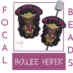 May include: Two black and brown cow-shaped beads with the text "ONE BOUIJEE HEIFER" in pink. The cow is holding a pink tumbler. A white and gray bead is attached to a metal rod. The word "BEADS" is written vertically.