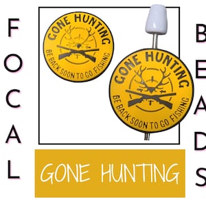 May include: Yellow and black hunting-themed bead with the text "GONE HUNTING" and "BE BACK SOON TO GO FISHING". The bead features a deer antler design and two crossed rifles. The bead is attached to a white pin.