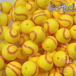 Puede incluir: Primer plano de un montón de cuentas amarillas en forma de pelota de softbol con costuras rojas. Las cuentas están dispuestas en un patrón aleatorio y todas son del mismo tamaño.