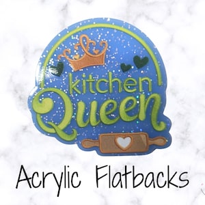 May include: A blue acrylic flatback with the words "Kitchen Queen" in green script, a gold crown, and a rolling pin with a heart. The flatback is sprinkled with glitter and has a light blue border. The text "Acrylic Flatbacks" is below.