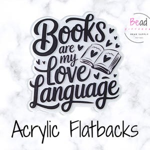 以下が含まれることがあります： 「Books are my Love Language」という黒い筆記体の文字が入った透明なアクリル製のフラットバック。デザインには、ハートの付いた開いた本と小さなハートのアクセントが含まれています。「Acrylic Flatbacks」という言葉が一番下にあります。