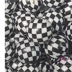 May include: A close-up of a pile of black and white checkered acrylic beads. The beads are round and have a glossy finish. The word "ACRYLIC" is written vertically in black letters on the left side of the image.