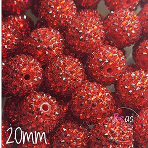 May include: Close-up of a pile of red, rhinestone-covered beads. Each bead is approximately 20mm in diameter and has a hole for stringing. The beads are a vibrant, sparkling red.