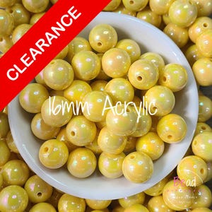 May include: A collection of iridescent yellow 16mm acrylic beads. The beads are inside a white bowl, with some spilling out. A red banner in the upper left corner reads "CLEARANCE". The beads have a pearlescent sheen and are suitable for jewelry making.