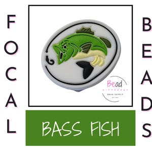May include: A white oval charm with a green and yellow bass fish design. The charm has a black outline and the text "Bead Bittersweet Bead Supply" is printed on the bottom.