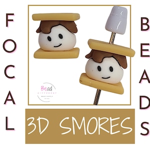 May include: A pair of 3D s'mores earrings. Each earring features a brown chocolate layer, a white marshmallow with a smiley face, and a golden graham cracker. The earrings are on a gold wire.