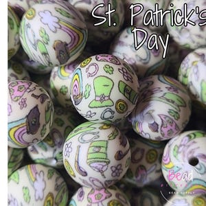 May include: Cream-colored round beads with St. Patrick's Day themed designs. The beads feature illustrations of rainbows, shamrocks, leprechaun hats, and other festive symbols in pastel colors. The text "St. Patrick's Day" is visible.