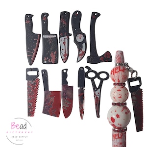 Può includere: Una collezione di ciondoli e perline a tema horror neri e rossi. I ciondoli includono coltelli, seghe e un'ascia, tutti con effetto splatter di sangue. Una penna con perline presenta la parola "HELP" e perline splatter di sangue.