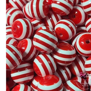 May include: A close-up of a pile of red and white striped acrylic beads. The beads are round with a hole through the center. The text "Acrylic" is written vertically on the left side of the image.