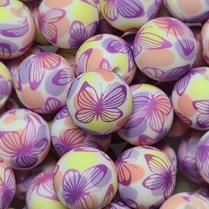 May include: A collection of colorful, round beads with a butterfly pattern. The beads are white with pink, purple, and yellow accents. The butterflies are purple with pink accents.
