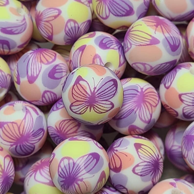 May include: A collection of colorful, round beads with a butterfly pattern. The beads are white with pink, purple, and yellow accents. The butterflies are purple with pink accents.