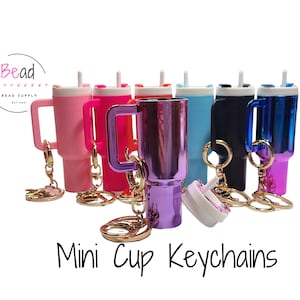 May include: A set of mini cup keychains in various colors, including pink, red, purple, blue, and black. Each keychain features a small cup with a handle and a straw, and a gold chain.