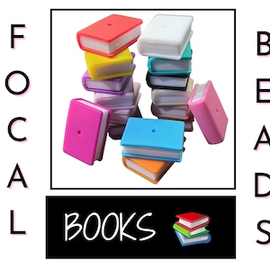 May include: A collection of colorful book-shaped beads in various colors, including red, yellow, pink, blue, and white. The word "BOOKS" is displayed in a black rectangle, with the words "FOCAL BEADS" arranged vertically on either side.