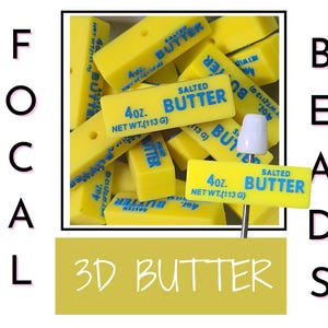 May include: A collection of rectangular yellow beads shaped like sticks of salted butter, each featuring blue text that reads 4oz. SALTED BUTTER NET WT. (113 G). One bead is mounted on a white pin, and the word FOCAL BEADS 3D BUTTER appears in the frame.