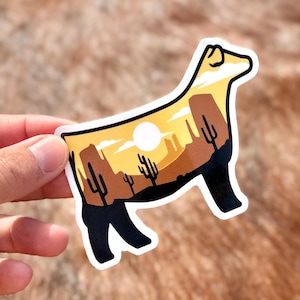 May include: A die-cut sticker in the shape of a dog, featuring a desert landscape scene. The sticker has a white border, with a yellow and brown desert scene inside the dog's silhouette. The scene includes cacti, mountains, and a sun.