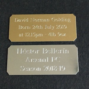 May include: Two gold and silver plaques with engraved text. The gold plaque reads "David Norman Golding Born: 24th July 2019 at 12.15pm - 4lb 9oz". The silver plaque reads "Héctor Bellerin Arsenal FC Season 2018-19".