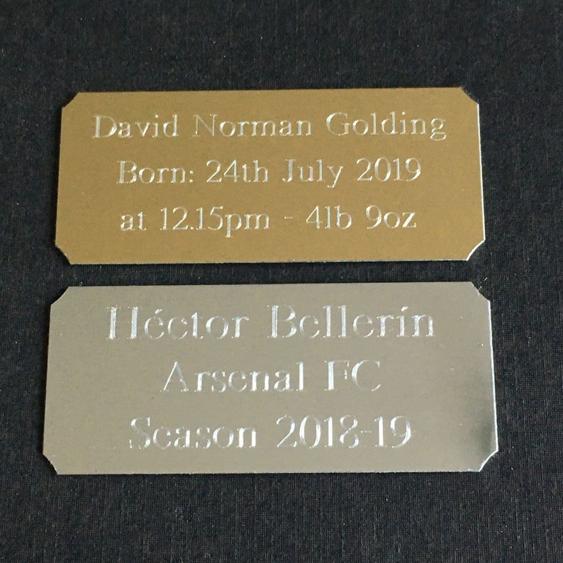May include: Two gold and silver plaques with engraved text. The gold plaque reads "David Norman Golding Born: 24th July 2019 at 12.15pm - 4lb 9oz". The silver plaque reads "H&eacute;ctor Bellerin Arsenal FC Season 2018-19".