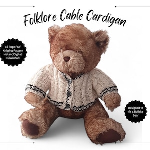 May include: A brown teddy bear wearing a cream-colored cable knit cardigan with black trim. The image includes text that reads "Folklore Cable Cardigan" and "Designed to fit a Build a Bear."