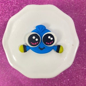 May include: A blue and yellow cartoon fish with big eyes and a smile. The fish is made of polymer clay and is about 2 inches tall.