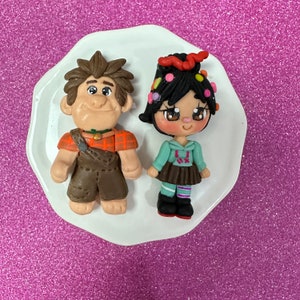 May include: A pair of handmade clay figurines of Wreck-It Ralph and Vanellope von Schweetz from the Disney movie Wreck-It Ralph. The figurines are painted in bright colors and have detailed features.