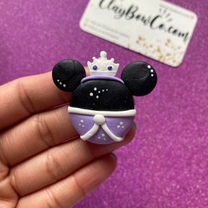 May include: Purple and black clay charm with a white crown and white dots. The charm is shaped like Mickey Mouse's head.