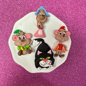 May include: A set of four hand-painted figurines featuring a black cat, a girl with a blue hat, and two mice. The figurines are on a white plate with a scalloped edge.