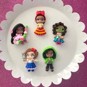 May include: Five colorful handmade polymer clay figurines of people with different hairstyles and outfits. The figurines are on a white plate with a scalloped edge.