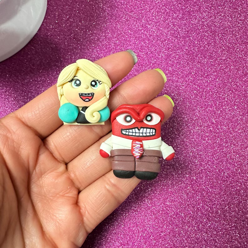 May include: Two handmade polymer clay figurines. One is a blonde woman with a teal jacket and black top. The other is a red character with a white shirt, brown pants, and a red tie. Both are smiling.