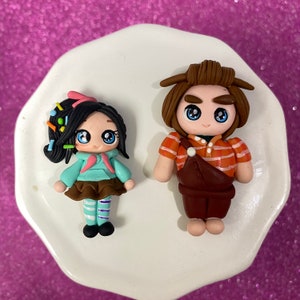May include: Two handmade polymer clay figurines of characters from the movie Wreck-It Ralph. The female figurine is wearing a blue and brown outfit with a pink bow in her hair. The male figurine is wearing a brown and orange outfit with brown hair.