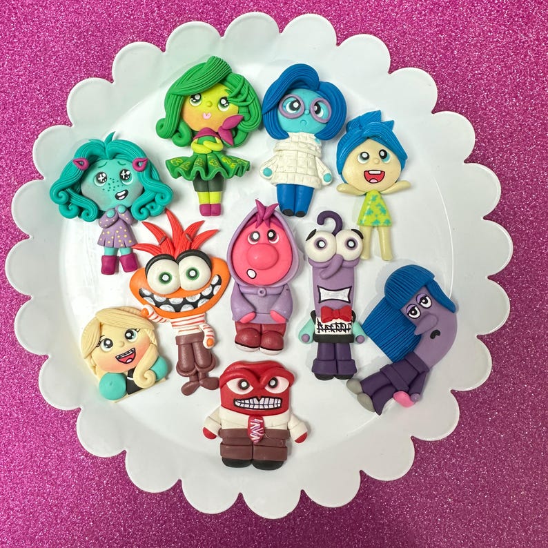 May include: A collection of colorful clay figurines of characters from the animated movie "Inside Out" arranged on a white scalloped-edge plate. The figurines feature various emotions, including Joy, Sadness, Anger, Fear, and Disgust, with detailed facial expressions and clothing.