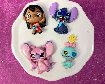 Könnte beinhalten: Vier Figuren aus dem Zeichentrickfilm Lilo & Stitch sind auf einem weißen, wellenförmigen Teller angeordnet. Die Figuren sind Lilo, Stitch, Angel und Scrump. Die Figuren sind hell gefärbt und aus hartem Material.