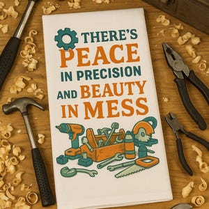 May include: White hand towel with the text "THERE'S PEACE IN PRECISION AND BEAUTY IN MESS" and a toolbox graphic. The towel is surrounded by tools like hammers, pliers, and a wrench, with wood shavings scattered around.