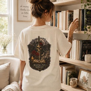 Peut inclure: Un t-shirt à manches courtes de couleur crème avec un motif détaillé au dos. Le dessin représente un crâne ailé, une épée, des roses rouges, une bougie allumée et un livre ouvert, avec le texte "READING PAST MIDNIGHT" imprimé en dessous.