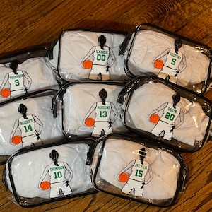 May include: Eight clear plastic zippered pouches with black trim. Each pouch features a white basketball player with a different name and number on the back. The names and numbers are: Thompson 3, Vance 00, Godfrey 5, Rooney 14, Mondone 13, Soda 20, Thompson 10, and Meyer 15.