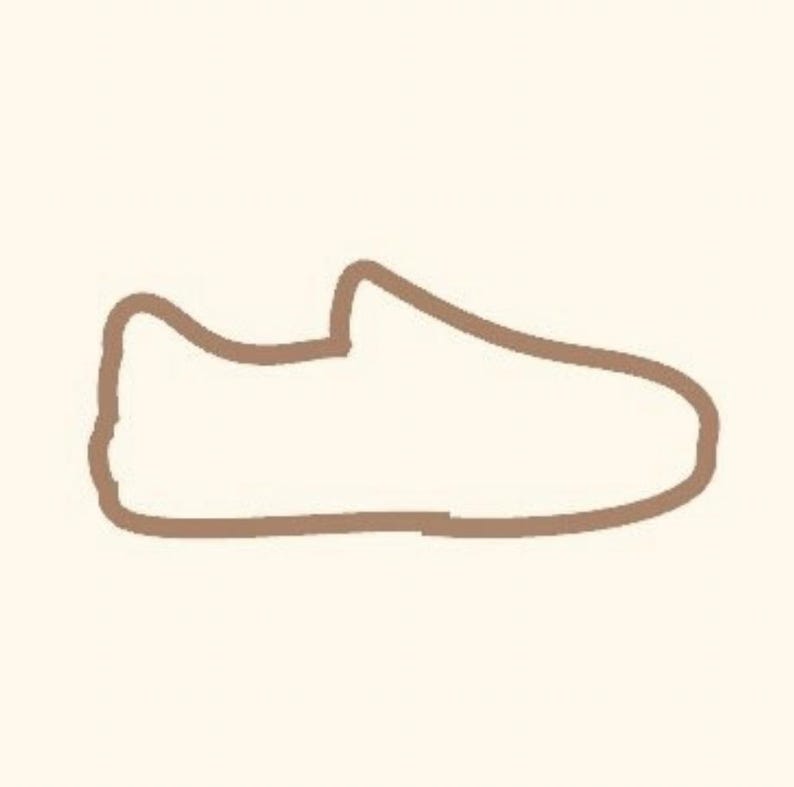 Puede incluir: Un dibujo lineal marr&oacute;n de un zapato. El zapato tiene una punta redondeada y un dise&ntilde;o de corte bajo, lo que sugiere un estilo casual. El contorno es grueso y el fondo es de color beige claro.