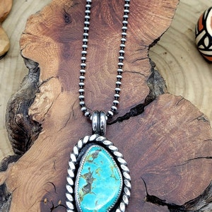 May include: A silver chain necklace with a turquoise stone pendant. The pendant is oval shaped and has a silver rope design around the edge.