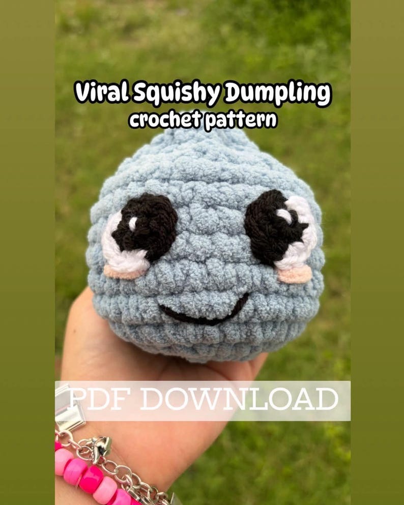 May include: A light blue crocheted dumpling with black and white eyes and a smiling mouth. The text "Viral Squishy Dumpling crochet pattern" is displayed at the top, and "PDF DOWNLOAD" is at the bottom.