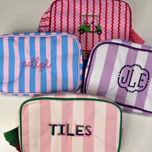 Pu&ograve; includere: Quattro trousse rettangolari con motivi a righe rosa, blu e viola. Una borsa ha un carrello da golf ricamato. Altre borse hanno testo e iniziali ricamate. Ogni borsa ha una chiusura con cerniera.