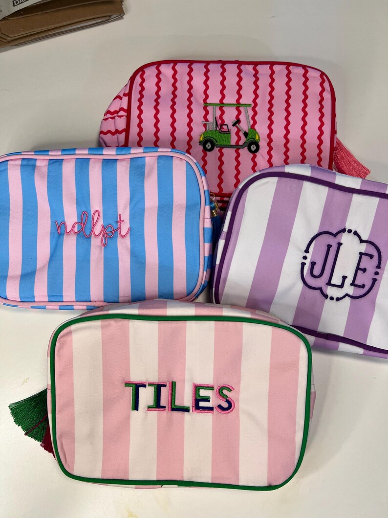 Pu&ograve; includere: Quattro trousse rettangolari con motivi a righe rosa, blu e viola. Una borsa ha un carrello da golf ricamato. Altre borse hanno testo e iniziali ricamate. Ogni borsa ha una chiusura con cerniera.