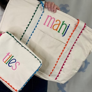 May include: A cream-coloured canvas tote bag and a matching smaller pouch, both featuring colourful scalloped trim in blue, orange, and pink. The tote is embroidered with the word "mahi" and the pouch with the word "tiles" in multi-coloured lettering.