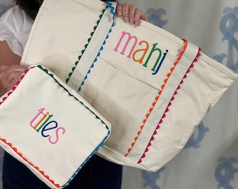 May include: A cream-colored canvas tote bag and a matching smaller pouch, both featuring colorful scalloped trim in blue, orange, and pink. The tote is embroidered with the word "mahi" and the pouch with the word "tiles" in multi-colored lettering.
