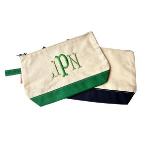 May include: Two canvas zipper pouches. One is cream-colored with a green bottom and embroidered green initials "IpN". The other pouch is cream-colored with a navy blue bottom. Both have a small green tab.