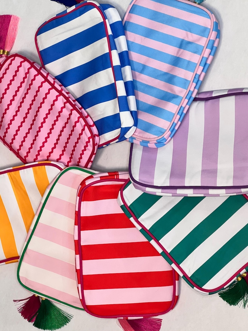Pu&ograve; includere: Una collezione di trousse per cosmetici a righe colorate. Le borse presentano varie combinazioni di colori, tra cui rosa, blu, rosso, verde e arancione, con strisce bianche. Ogni borsa ha un bordo a contrasto e un nappa.