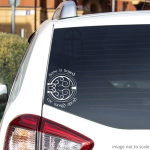 May include: White vinyl decal sticker with a circular design and the text "Home is behind, the world ahead". The sticker is applied to the rear window of a white car.