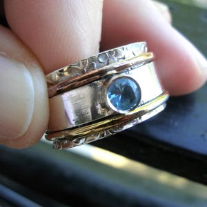 Peut inclure: Une bague tournante en argent avec une pierre précieuse bleue et des accents dorés.